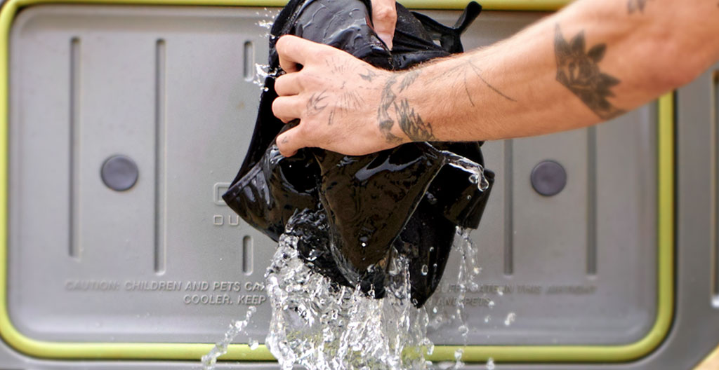 Gros plan sur des mains faisant couler de l'eau sur un gilet réfrigérant sous un robinet dans un vestiaire industriel